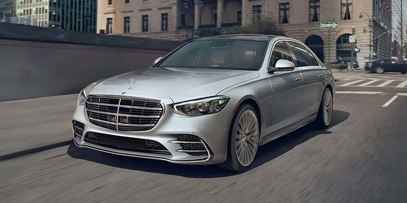 A silver Mercedes-Benz sedan drives through a downtown street.